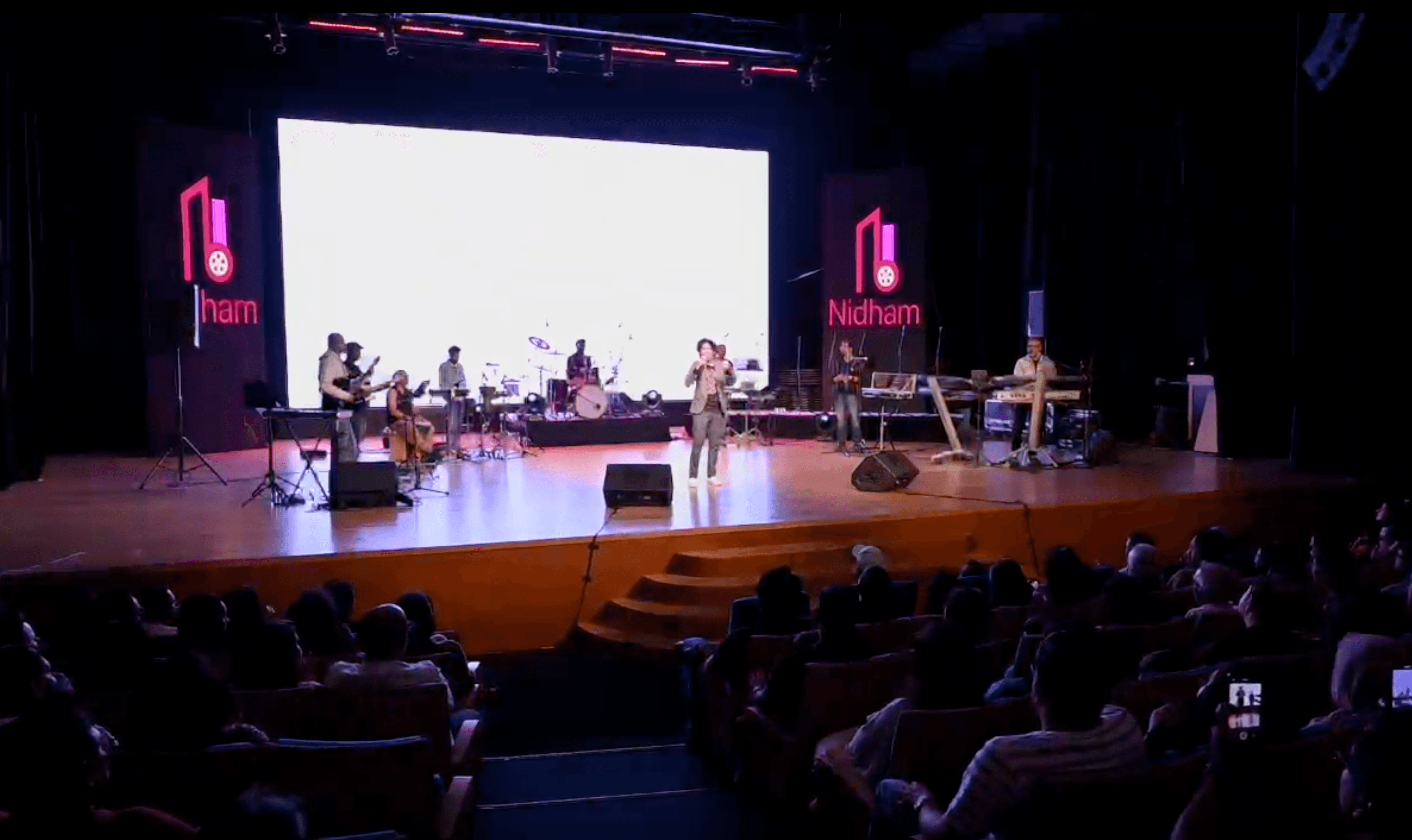 Live band and vocalist performing on stage under a Nidham-branded backdrop